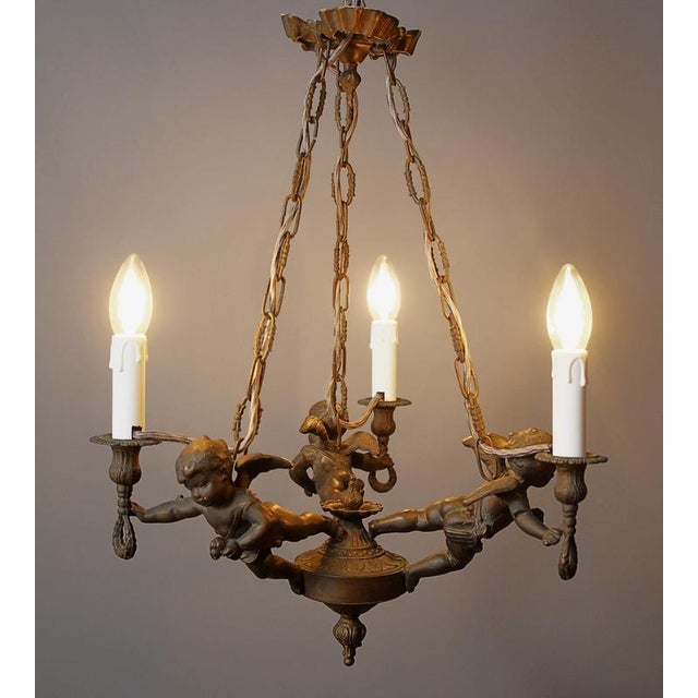 Decorative baroque chandelier made of bronze, decorated with plastic putti figures that carry individual light arms. The...