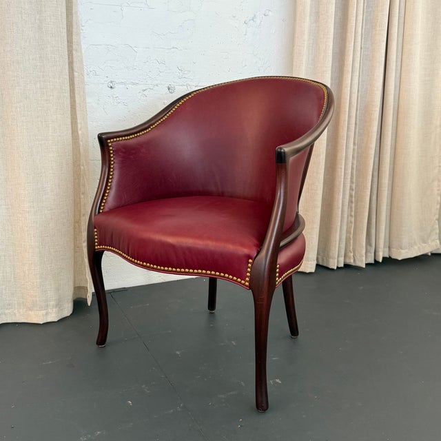 This classic library tub armchair circa the 1940s showcases a handsome barrel silhouette upholstered in a rich burgundy...