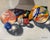 This oil on linen panel depicts a playful arrangement of colorful marbles and crayons emerging from an open box, casting...
