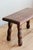 Low, rectangular stool in dark wood, resting on four turned legs with the typical curve of rustic furniture. Antique or...