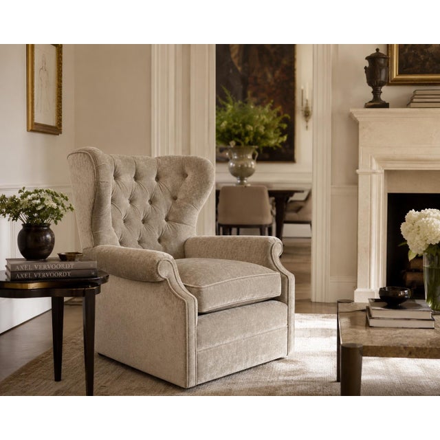 An upholstered wingback armchair featuring a deep button-tufted backrest, rolled arms, and a skirted swivel base. The...