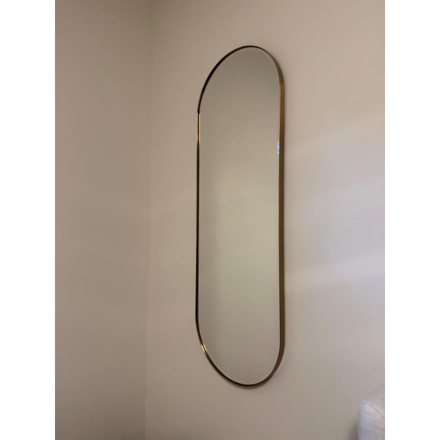 Edged with a slim brass band, this minimalist wall mirror curves an elongated oval for a modern and elegant silhouette....