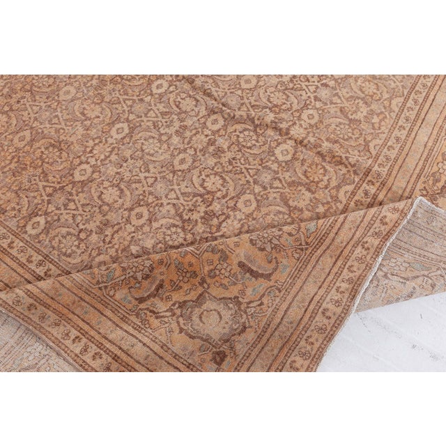 This circa-1920 antique Persian Tabriz rug features a densely patterned all-over design of herati patterns in brown and...