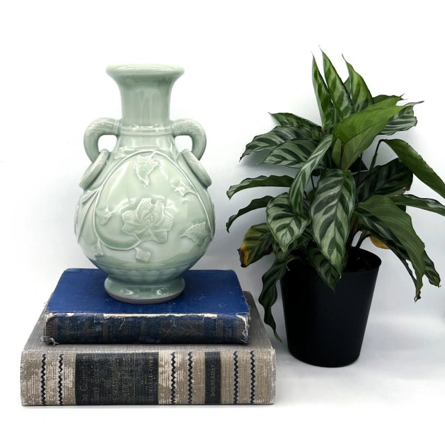 A refined mid-20th-century celadon porcelain vase featuring elegant floral reliefs and distinctive looped side handles....
