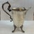 Victorian silver plate pitcher with claw foot legs and heavily decorated handle. The pitcher flares from the bottom up and...
