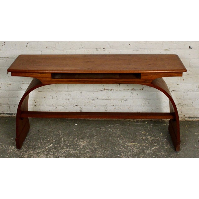 This is a stunning mid-century teak console table. The table top is supported by beautiful bent wood legs that form an...