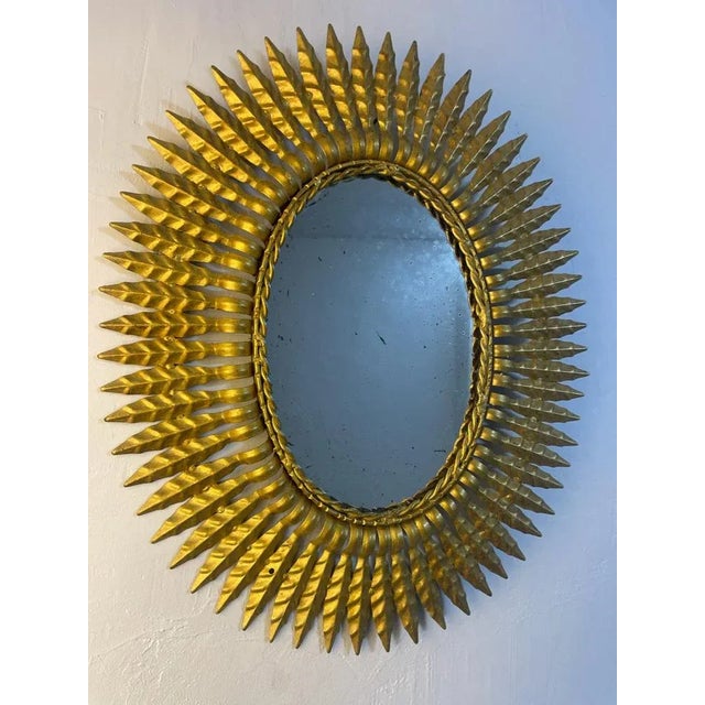 Large oval sun mirror in wrought iron from the 1950s. Italian artisanal fabrication, decor of leaves, gold color.