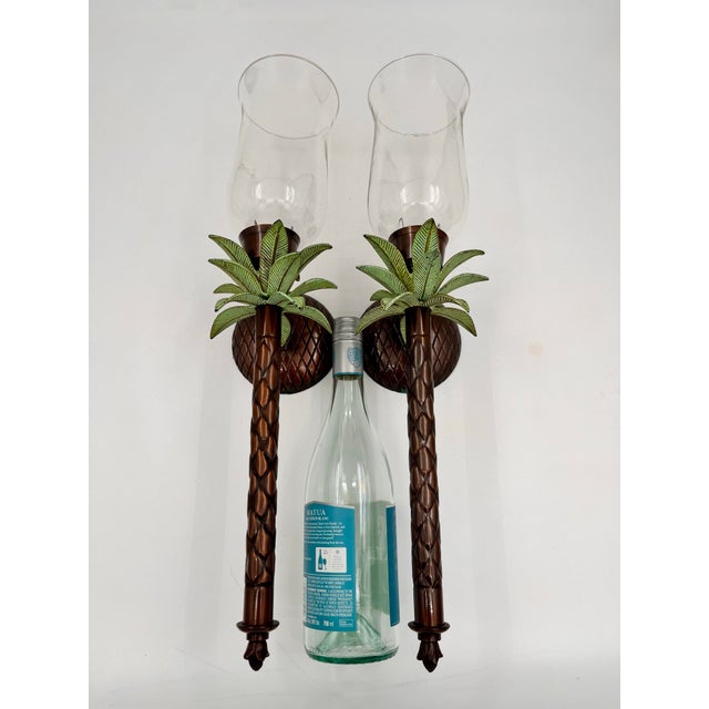 Striking pair of vintage metal palm tree wall candle sconces, each topped with a clear glass hurricane shade that...