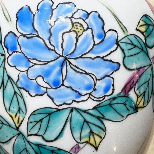 A small white chinoiserie ginger jar with a lid. The body and lid are both decorated with hand-painted blue and pink...