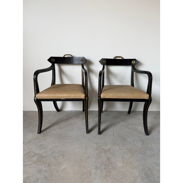 Elegant pair of John Gee style Hollywood Regency armchairs featuring dramatic ebonized wood frames, graceful saber legs,...