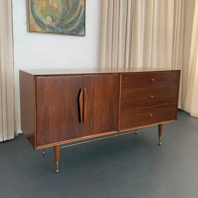 This stunning walnut and brass credenza dresser is attributed to Kent Coffey, circa 1950s. This credenza is the epitome of...