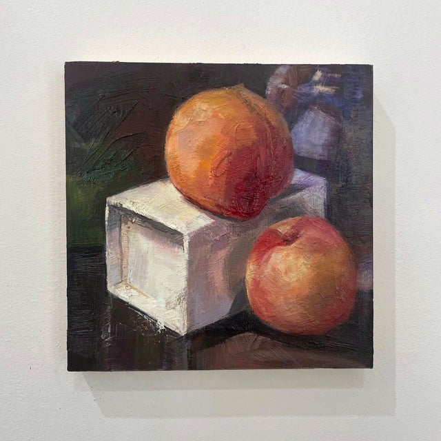 This oil on board painting presents two peaches resting atop a simple white cube, creating a striking contrast between the...