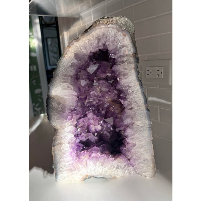 A striking natural amethyst cathedral geode featuring richly saturated purple crystal formations that transition...