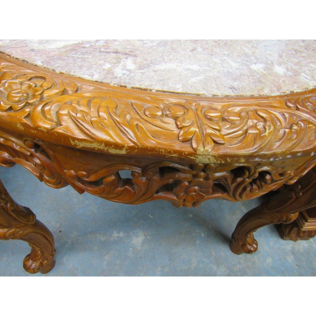A striking round carved wood table featuring an inset pink and cream marble top surrounded by an exceptionally detailed...
