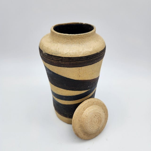 Hand-thrown stoneware lidded vessel with bold diagonal black stripes on raw unglazed clay body, fitted disc lid, and dark-...