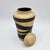 Hand-thrown stoneware lidded vessel with bold diagonal black stripes on raw unglazed clay body, fitted disc lid, and dark-...
