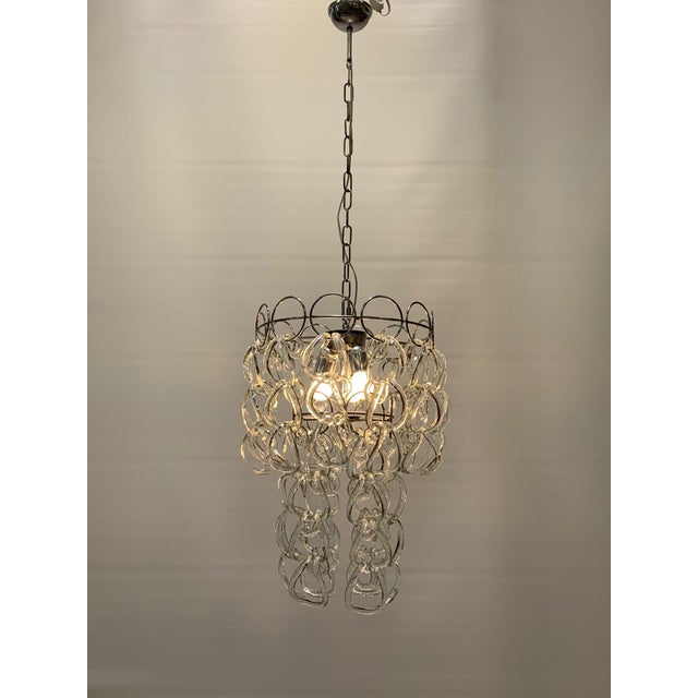 This pendant lamp features an elegant and dramatic design, composed of a circular metal structure with a polished finish...