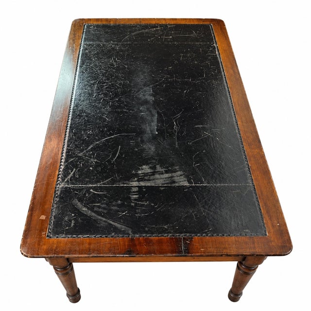This antique writing table featuring an inset black leather writing surface framed in richly toned wood. The leather top...