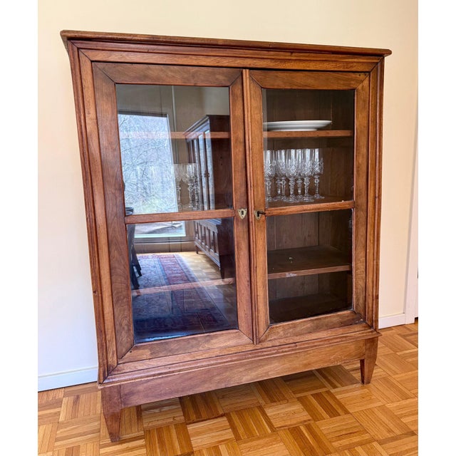 An unpretentious antique walnut bookcase or vitrine display cabinet with a lovely wood grain patina, two glass-paneled...