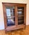 An unpretentious antique walnut bookcase or vitrine display cabinet with a lovely wood grain patina, two glass-paneled...