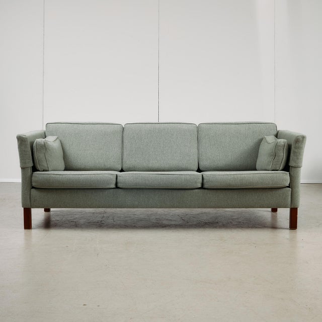 This mid-century three-seater sofa pairs clean lines with thoughtful functionality. Supported by cherry wood legs, the...