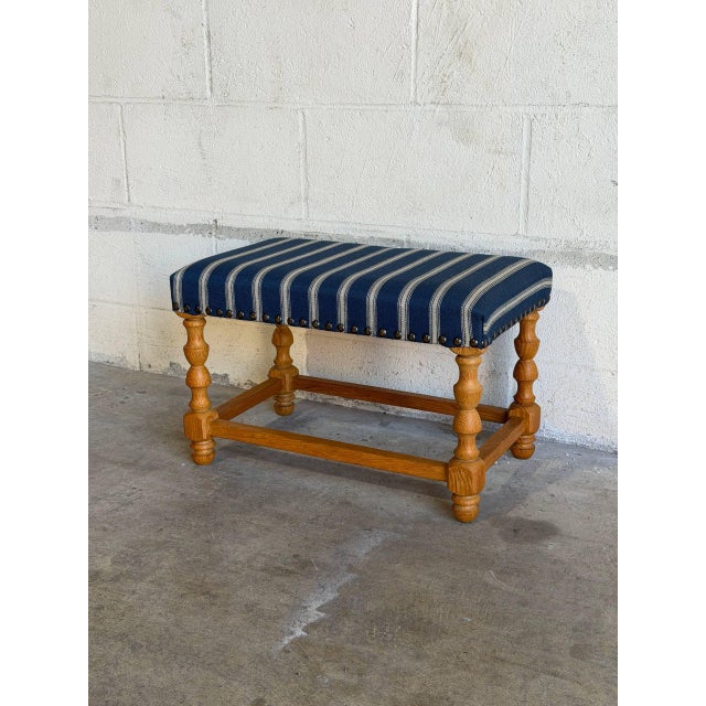 Featuring a cushioned rectangular top with brass nailhead trim, this ottoman rests on a turned wooden frame. Its...