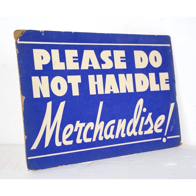 Vintage retail cardboard wall sign with a blue background and white lettering. The sign reads, Please Do Not Handle...