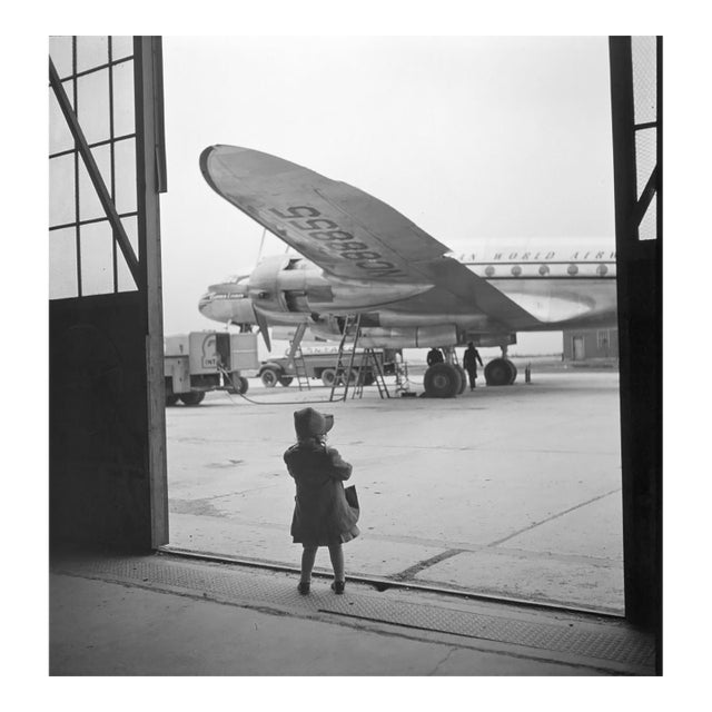 Young Traveller by Toni Frissell A young girl stands in her raincoat awaiting a plane to be refilled for her travels....
