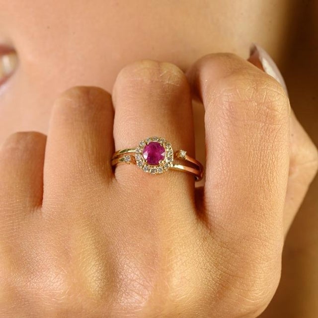 This vintage-inspired halo ring features a round-cut ruby totaling approximately 0.60 carats, elegantly set in 14K yellow...