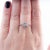 An 18k white gold engagement ring featuring a central white diamond weighing 0.18 carats. The diamond is cut in an Old...