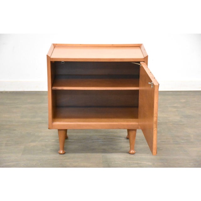 A mid century modern walnut nightstand with a single push to open door. Original condition. Some veneer damage shown....