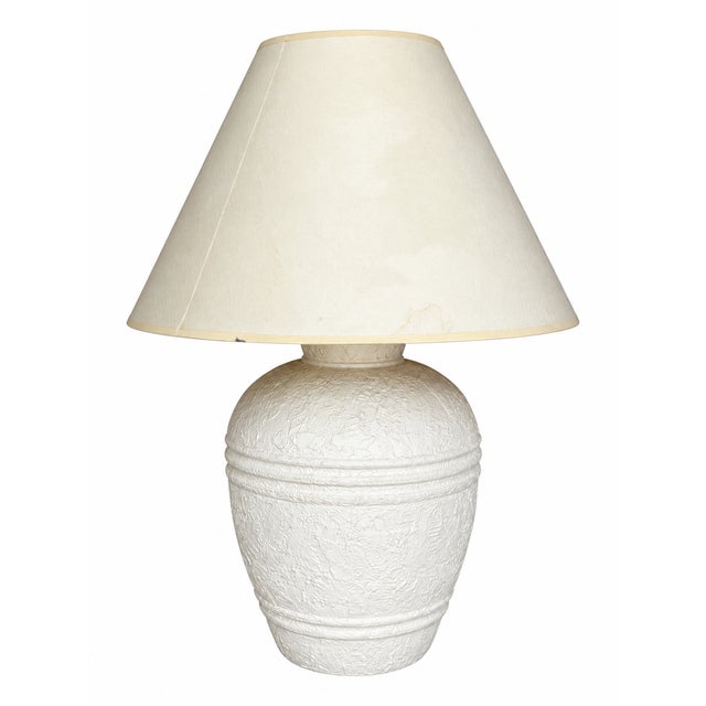 A sculptural urn-form table lamp featuring a richly textured white finish, rounded shoulders, and raised horizontal bands...