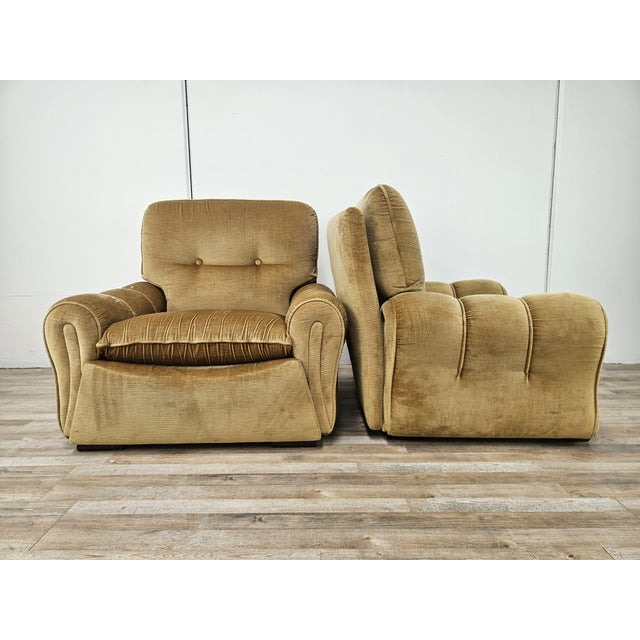 An authentic pair of 1970s armchairs with a soft and generous design, featuring wide rounded armrests, a deep seat, and...