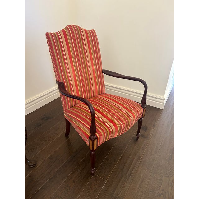 A stylish pair of high-back armchairs featuring classic silhouettes and eye-catching striped upholstery in rich red, gold,...