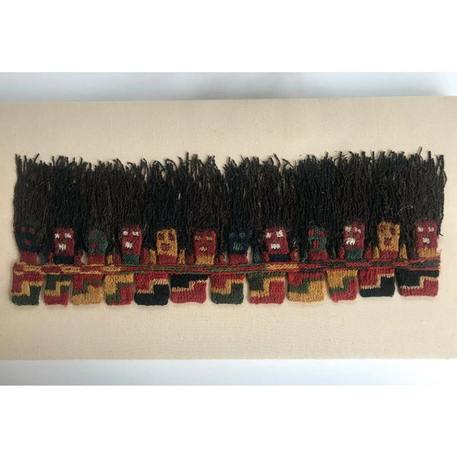 A Proto-Nazca textile fragment from Southern Peru, framed in a shadow box. It features a biomorphic faces typical of the...
