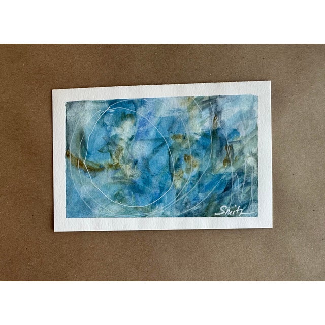 An ethereal abstract watercolor composition in layered shades of blue, aqua, and soft earth tones. Energetic white...