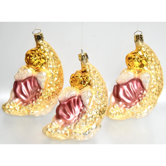 Three adorable large mouth blown-in-mould glass ornaments depicting an angel asleep on a crescent moon, hand decorated in...