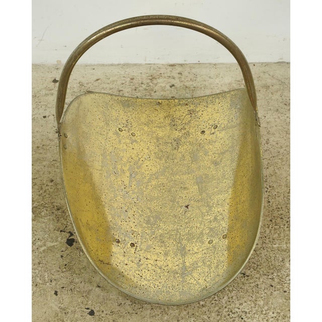 Vintage brass firewood log holder featuring a classic, curved scoop design with an overhead swing handle and decorative...