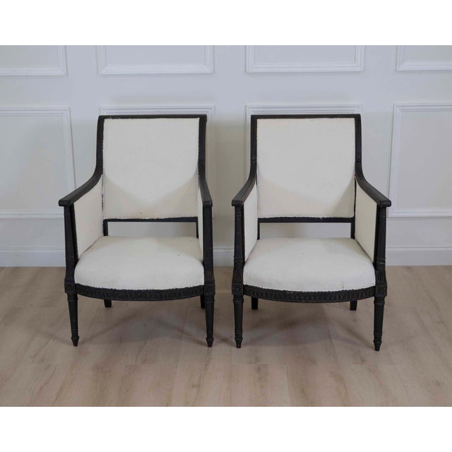 An elegant pair of Swedish Empire style armchairs featuring hand-painted black frames with carved neoclassical detailing....