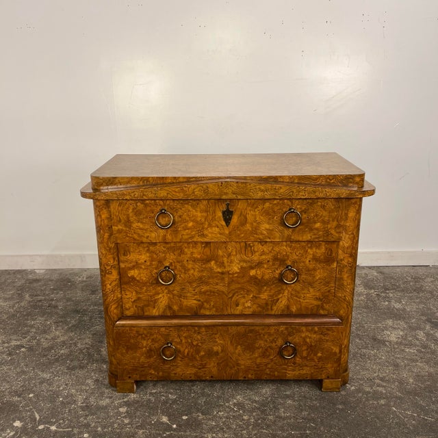 This is a neoclassical-style chest of drawers by Baker Furniture. It features three large drawers, gorgeous Burlwood...
