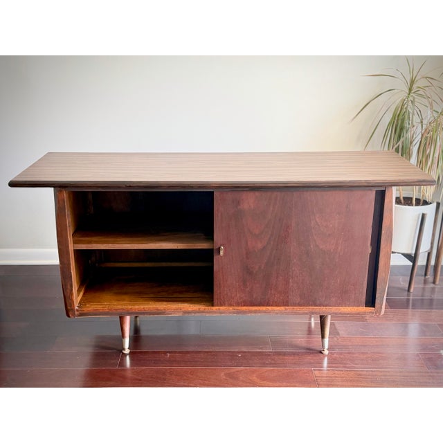 A vintage American Mid Century Modern walnut credenza featuring clean architectural lines, sliding doors, tapered legs...