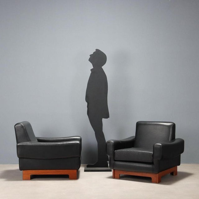 Two vintage armchairs with wooden frames and original black leather upholstery from the period. This piece is attributed...