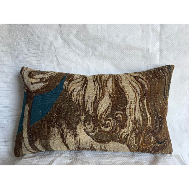 This elongated rectangular pillow features a richly woven tapestry design defined by fluid, layered forms that move...