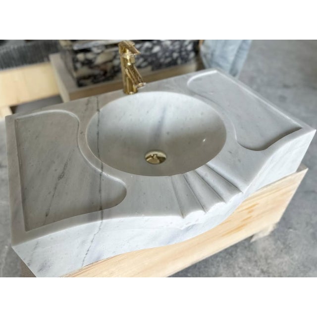 "Exquisitely hand-carved from a single block of natural white marble, this custom vanity sink features a signature fluted...