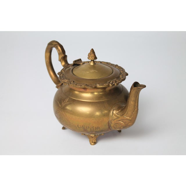 Vintage Middle Eastern etched brass teapot featuring a bulbous body, footed base, and etched palm tree and floral motifs....