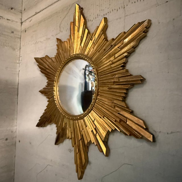 This striking mid-century giltwood starburst mirror features dynamically layered, hand-carved wooden rays finished in an...