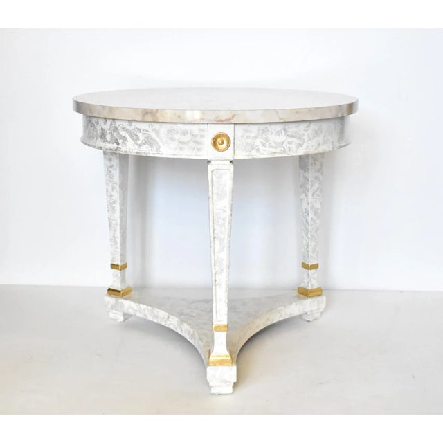 A vintage round, three-legged side table in a neoclassical style, with tapered legs, a faux marble laminate top in gray,...