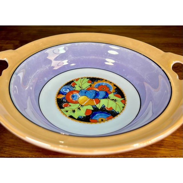Peach colored lusterware bowl with a lavender interior, and a hand painted central medallion in vibrant blue, green, and...