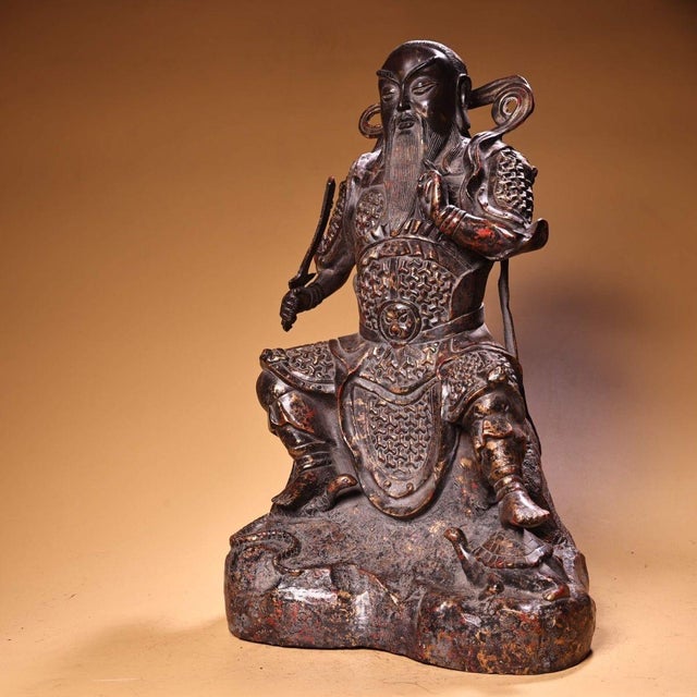 This is a cast bronze statue of a seated warrior deity, likely representing Guandi (the deified Guan Yu). The figure is...