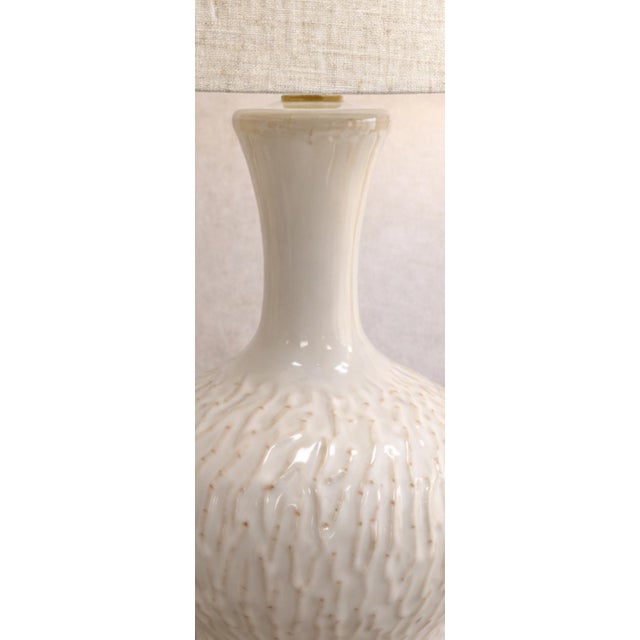 Elegant matching pair of cream glazed ceramic table lamps featuring a beautifully textured rounded base and neutral linen...
